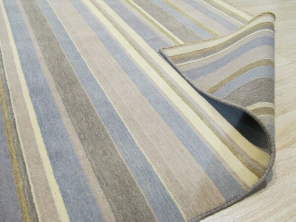 Close-up of a striped blue, taupe, and cream rug rolled back on a light wood floor.