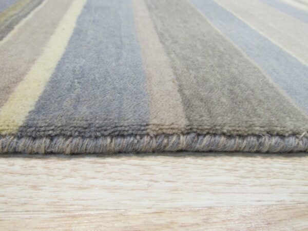 Striped rug in shades of blue, gray, and cream, showing the edge and medium pile on a light wood floor.