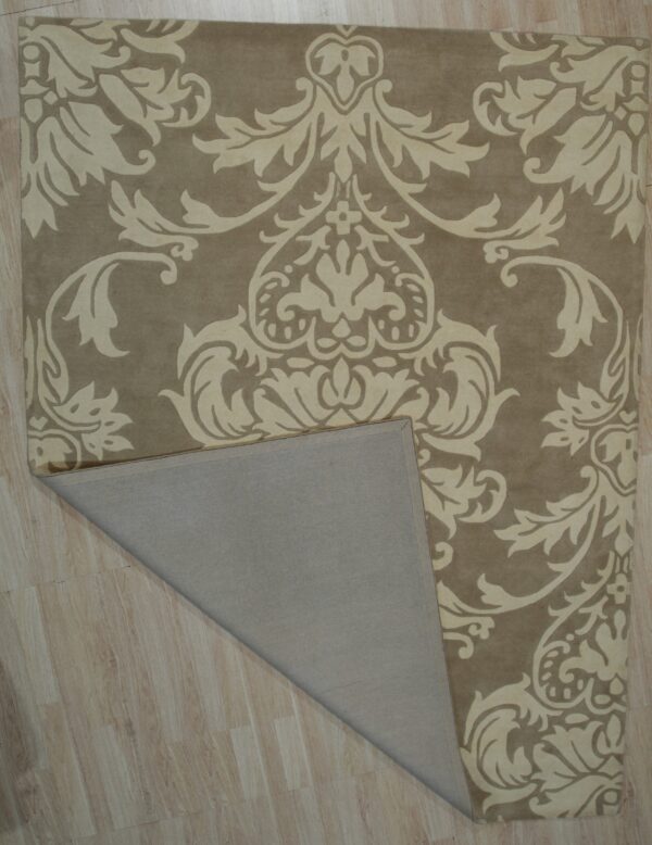 Beige rug with high-contrast light damask pattern lying on wood flooring, showing the folded gray backing.