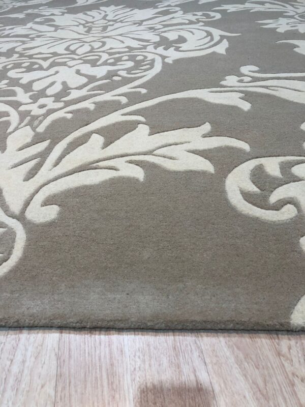A gray and cream high-low pile rug with a swirling damask pattern rests on light wood planks.