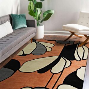 Terracotta, black, and beige abstract patterned rug placed beneath a grey sofa on wood floors.