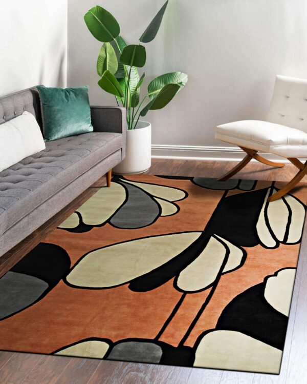Terracotta, black, and beige abstract patterned rug placed beneath a grey sofa on wood floors.