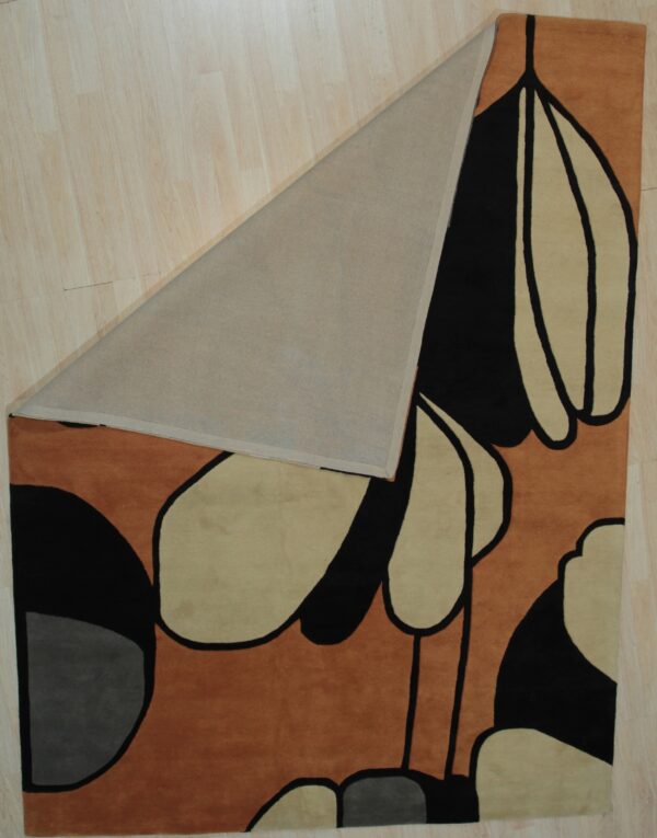 Low-pile rug in rust, black, and tan modern abstract pattern folded over light wood flooring.