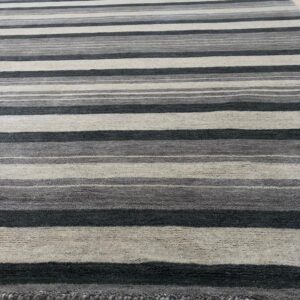 Grey, charcoal, and beige striped rug with textured pile rests on light wooden plank flooring.