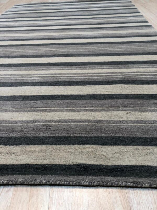 Grey, charcoal, and beige striped rug with textured pile rests on light wooden plank flooring.