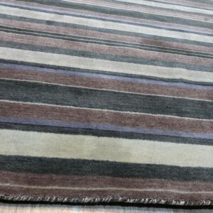 Striped rug with colors including charcoal, mauve, cream, and lavender rests on light wood planks.