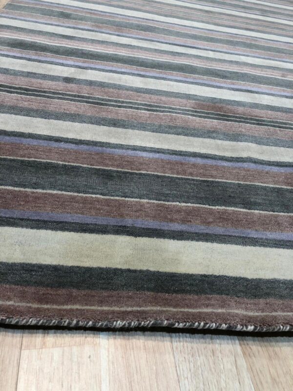 Striped rug with colors including charcoal, mauve, cream, and lavender rests on light wood planks.