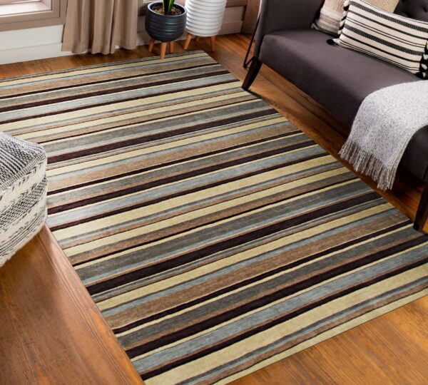 Brown, beige, and blue-gray striped rug rests on wood floors next to a dark sofa and patterned pouf.
