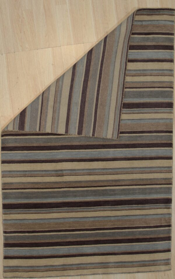 A striped rug in brown, blue, and tan is folded back on light wood flooring.
