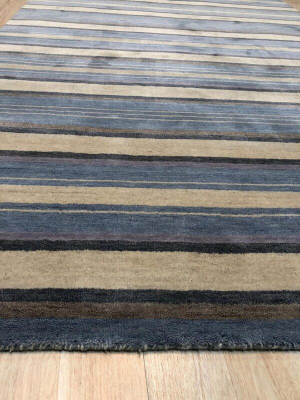 Low-angle view of a striped rug featuring blue, beige, gray, and brown colors on light wood flooring.