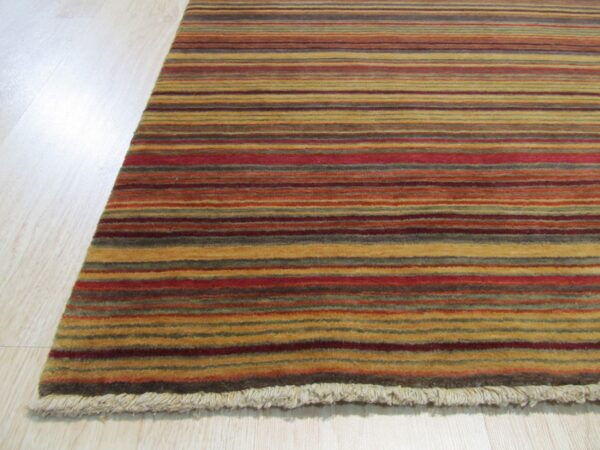 Close-up of a medium-pile rug featuring horizontal stripes in red, gold, brown, and green on light wood flooring.