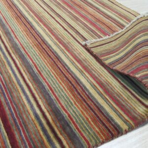 A multicolored striped rug in red, gold, purple, and green is rolled back on light wood flooring.