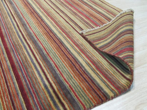 A multicolored striped rug in red, gold, purple, and green is rolled back on light wood flooring.