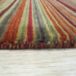 High-pile striped rug in rust, olive, and burgundy colors, lying on light blonde wood flooring.