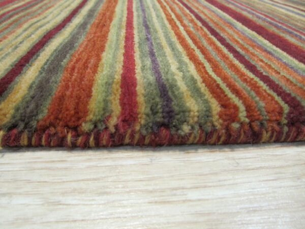 High-pile striped rug in rust, olive, and burgundy colors, lying on light blonde wood flooring.