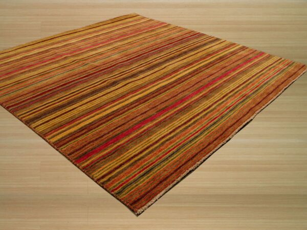 Warm-toned striped rug in gold, rust, and red hues covering light wood plank flooring.