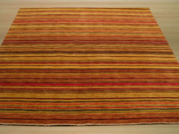 Striped area rug in warm tones of gold, red, and brown rests on light wood flooring.