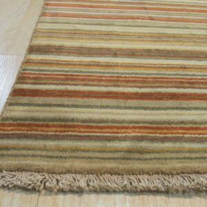 Earth-toned striped rug with beige, rust, and olive bands, showing a fringe detail on light wood flooring.