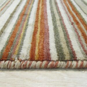 The rug edge and plush pile show vertical stripes of cream, terracotta, and olive green on light wood.