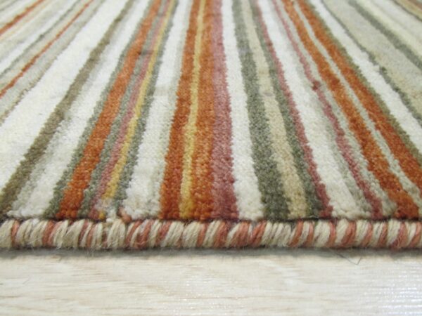 The rug edge and plush pile show vertical stripes of cream, terracotta, and olive green on light wood.