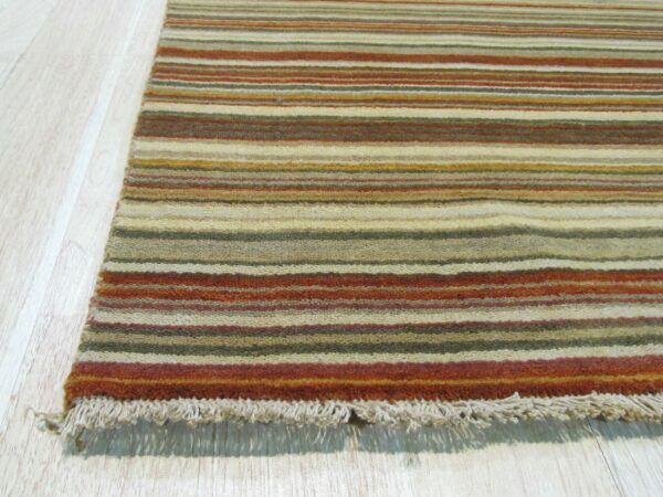 Low-pile rug with horizontal stripes in rust, gold, green, and beige rests on light wood floor showing fringe.