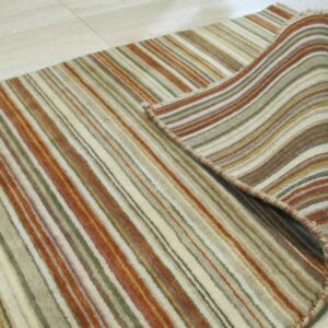 A striped rug in earthy tones of green, rust, and cream is partially rolled back on light flooring.