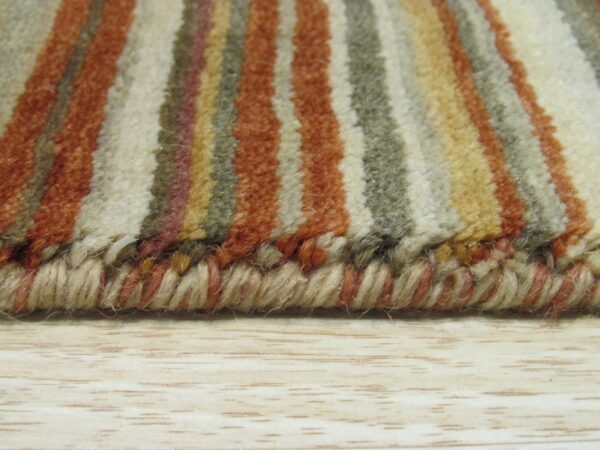 High-pile striped rug in rust, cream, and olive rests on light wood, showing the thick serged edge.