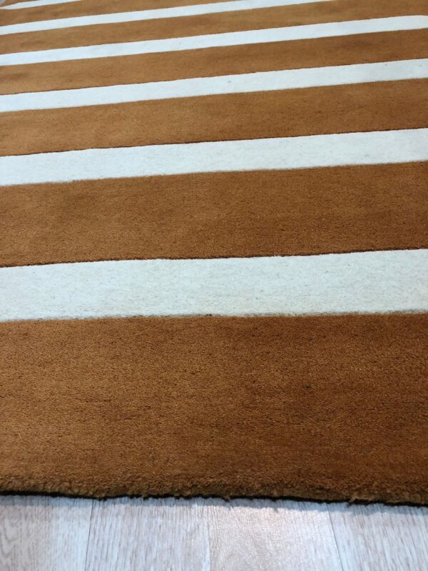 Brown and white striped rug with varying texture shown against light plank flooring.