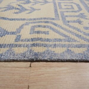 Close view of a textured cream and blue rug edge on light blonde wood planks.