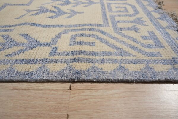 Close view of a textured cream and blue rug edge on light blonde wood planks.