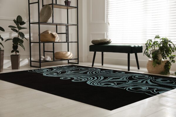 A black rug with a detailed teal swirling pattern rests on light wood in a bright room.