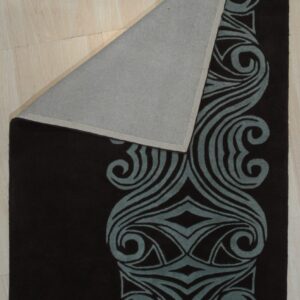 Dark brown rug with a prominent blue-gray swirling border design is folded over on light wood flooring.