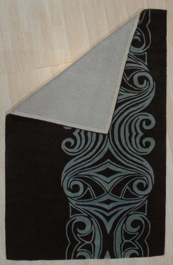 Dark brown rug with a prominent blue-gray swirling border design is folded over on light wood flooring.