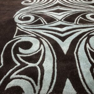 Plush dark brown rug featuring an elevated blue abstract scroll pattern on a light wooden floor.