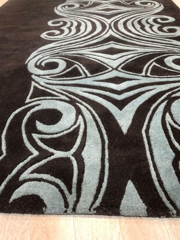 Plush dark brown rug featuring an elevated blue abstract scroll pattern on a light wooden floor.