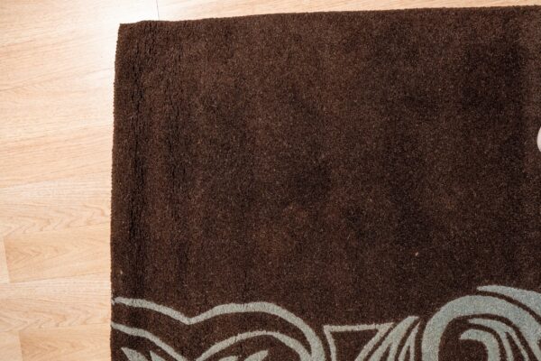 Textured dark brown rug featuring light blue curving lines rests on light blonde wood flooring.