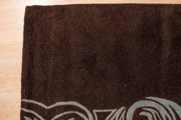 Textured brown rug with a stylized blue-gray border pattern rests on light wood planks.