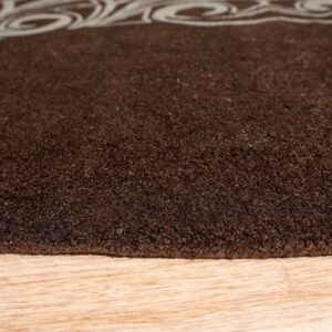 Dark brown high-pile rug with a light scroll pattern border lies on natural wood planks.