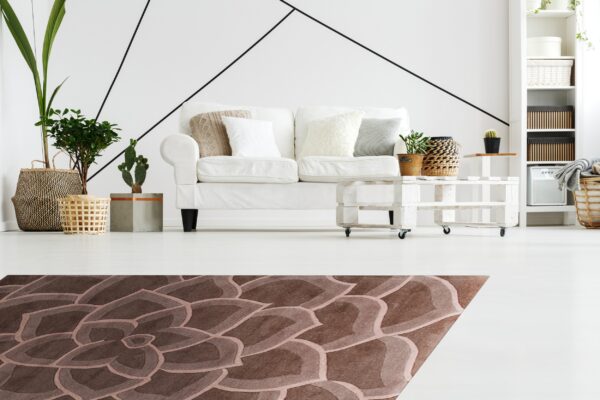 Brown carved rug with a large-scale petal design anchors a bright room with white furniture and plants.