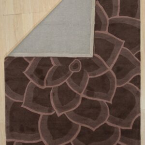 Dark brown carved rug with a repeating floral pattern, corner folded back revealing a gray underside on wood floor.