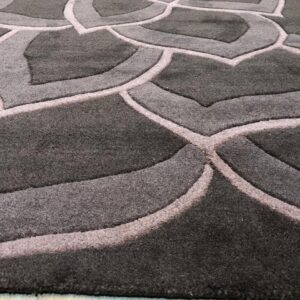 Plush dark gray rug featuring a carved light gray floral pattern rests on pale wood plank flooring.