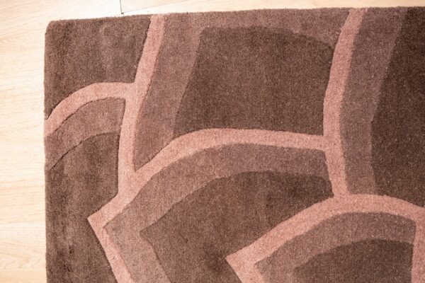 Textured dark brown rug with a lighter brown abstract curved pattern on light wood flooring.