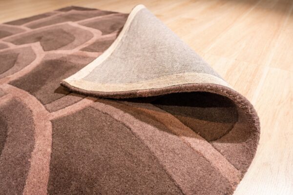 Rolled brown rug with an organic geometric pattern and carved pile on light wood flooring.