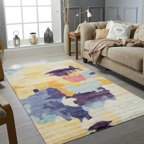 Low-pile abstract rug in purple, blue, yellow, and orange tones in a bright gray living room.