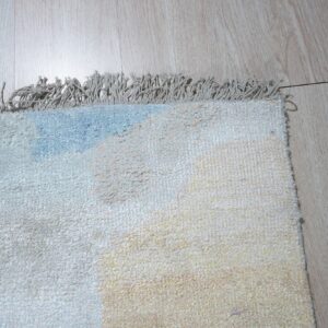 Lightly colored high-pile rug detail showing cream, pale blue, and yellow patches on wood planks.