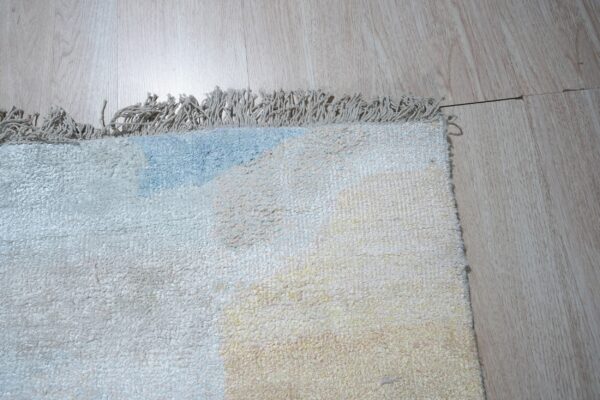 Lightly colored high-pile rug detail showing cream, pale blue, and yellow patches on wood planks.