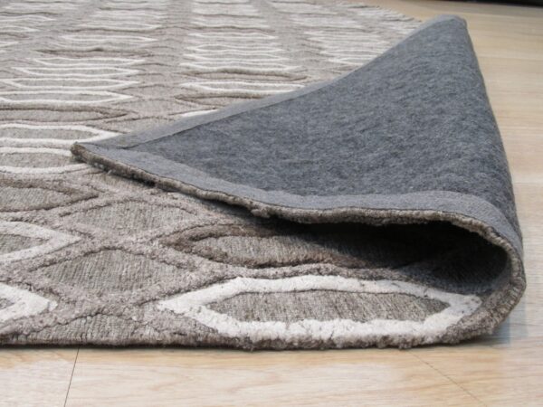 Neutral rug featuring a raised wavy pattern is rolled back, revealing its dark gray backing on wood flooring.