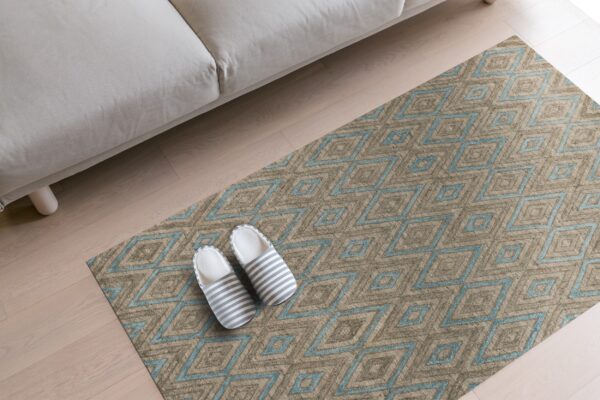 Tan and blue geometric diamond rug on wood floors with a beige sofa edge and striped slippers.