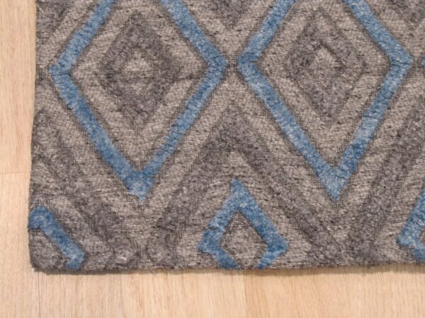 A textured gray rug featuring a raised blue diamond pattern rests on light blonde wood floorboards.