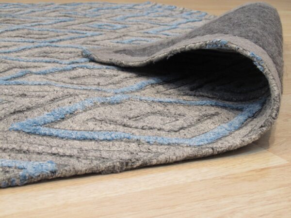 A rolled-back gray rug with bright blue zigzag lines rests on blonde wood flooring.